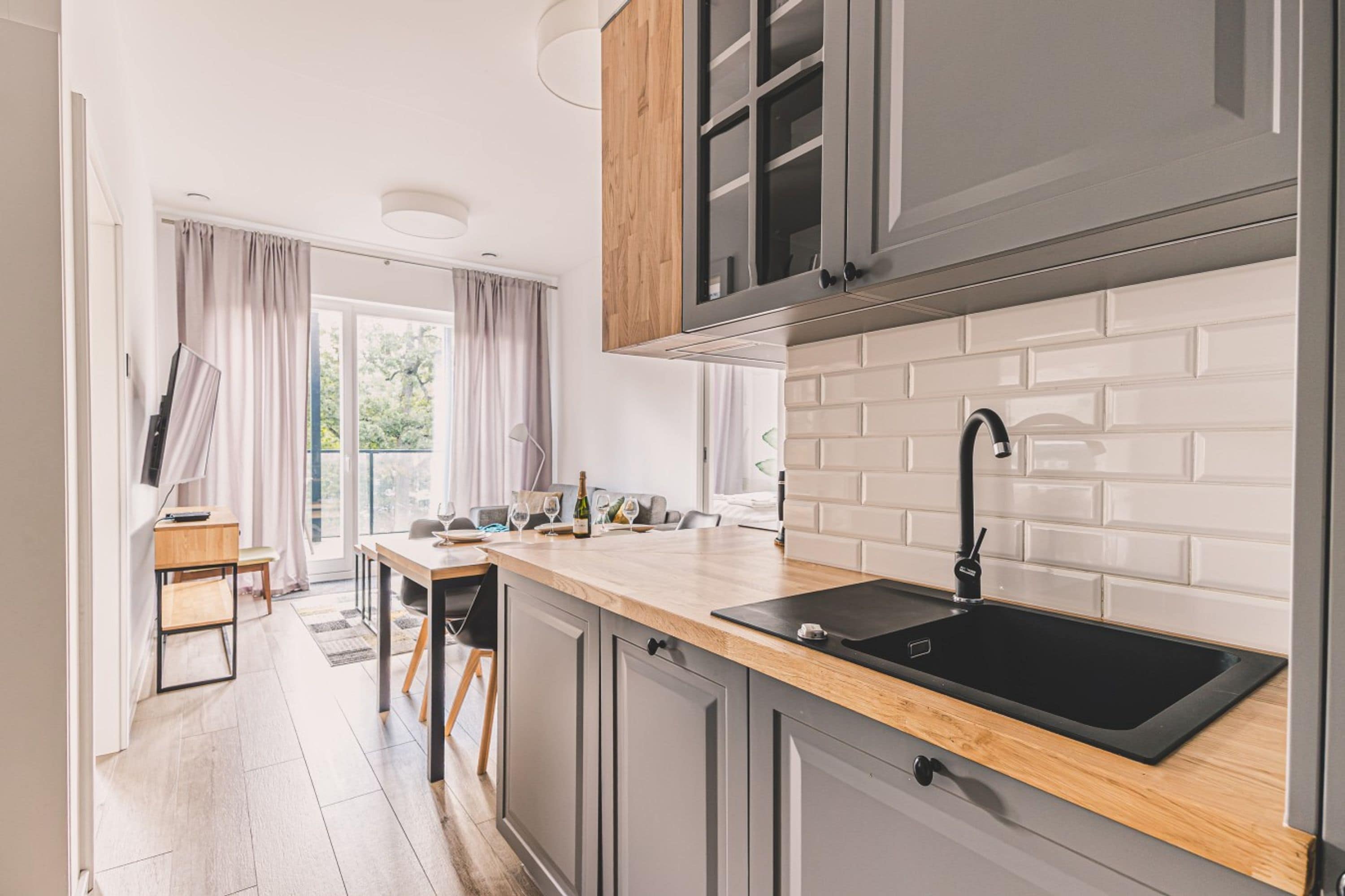 A modern kitchen with a wooden countertop, a black sink, and grey cabinets.