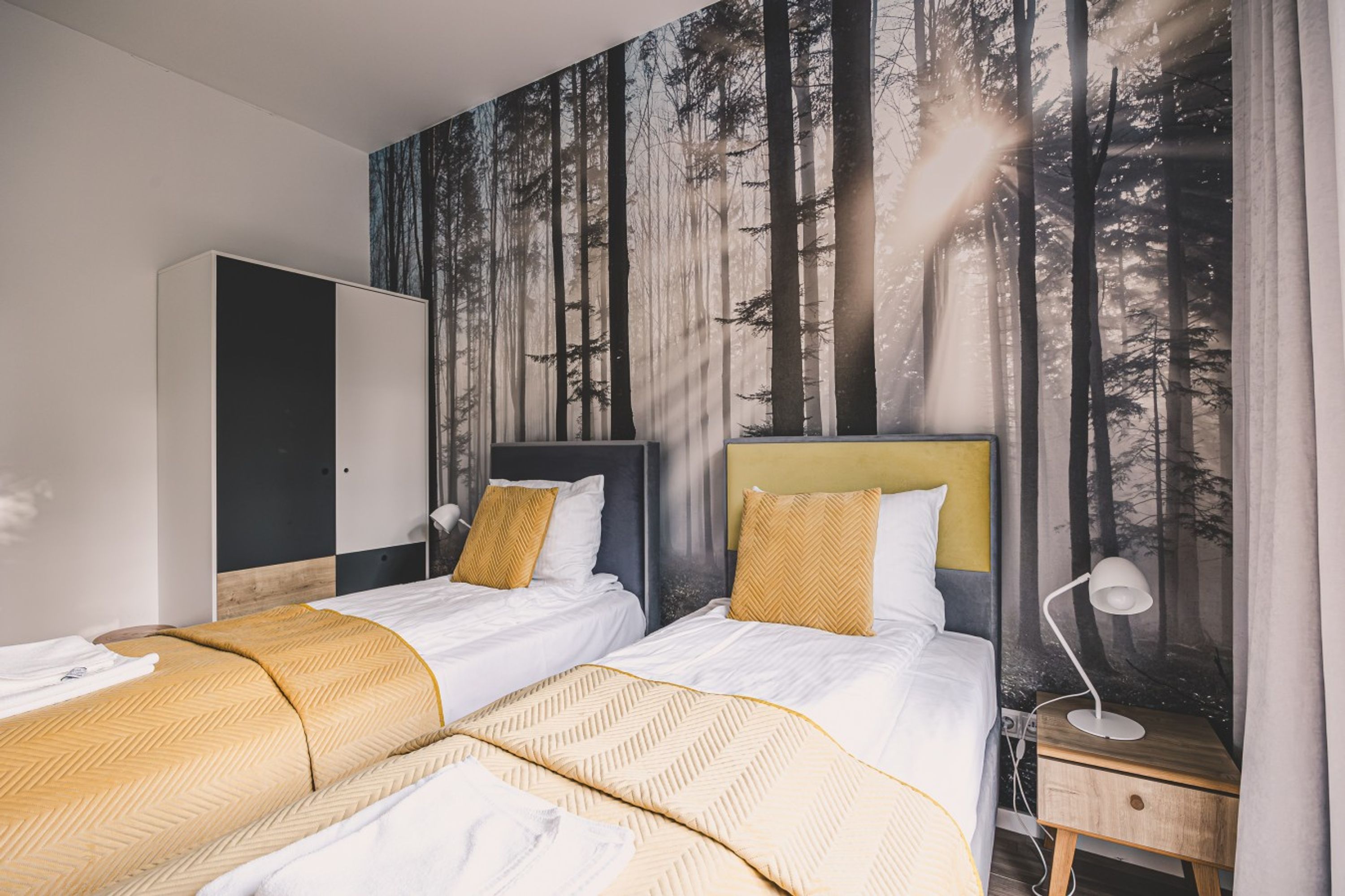 Un dormitorio con dos camas, un armario y un mural de un bosque.