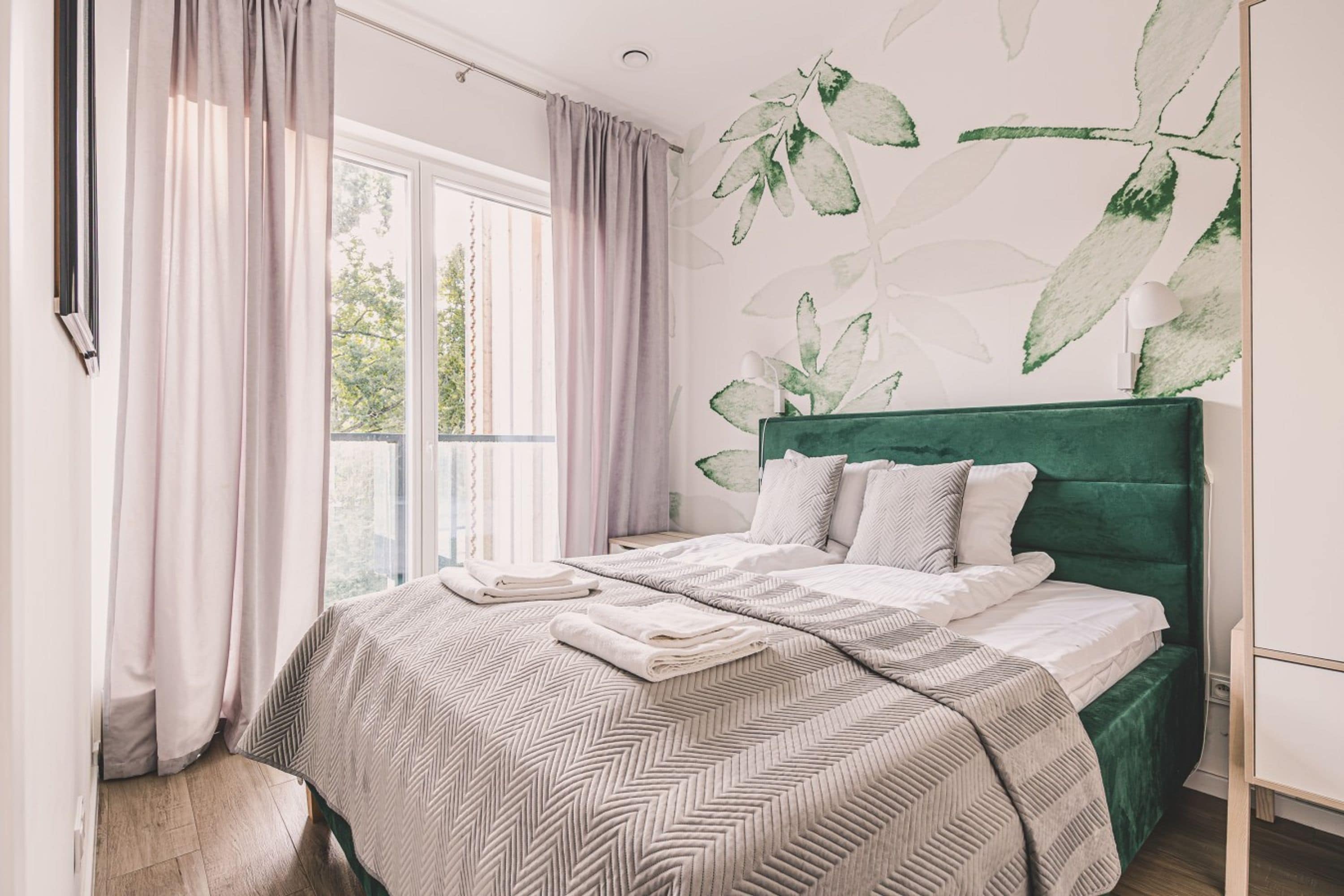 Un dormitorio con cama, cortinas, ventana y pared con ilustraciones de plantas.