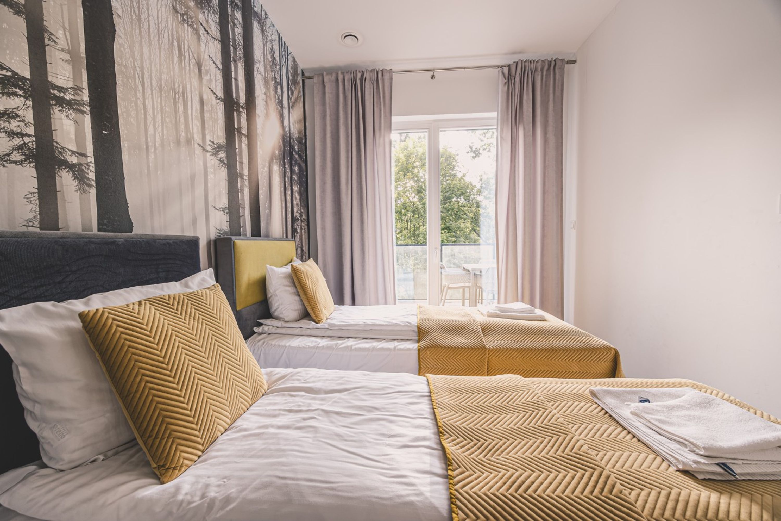 Habitación de hotel con dos camas, un ventanal con cortinas y vista a árboles.