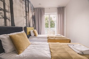 Une chambre d’hôtel avec deux lits, une grande fenêtre avec des rideaux et une vue sur les arbres à l’extérieur.