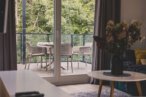 A balcony with a table and chairs, a potted plant, and a view of trees.