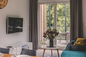 A modern living room with a flat-screen TV mounted on the wall, a white console table, a round coffee table, and a teal sofa with a yellow pillow.