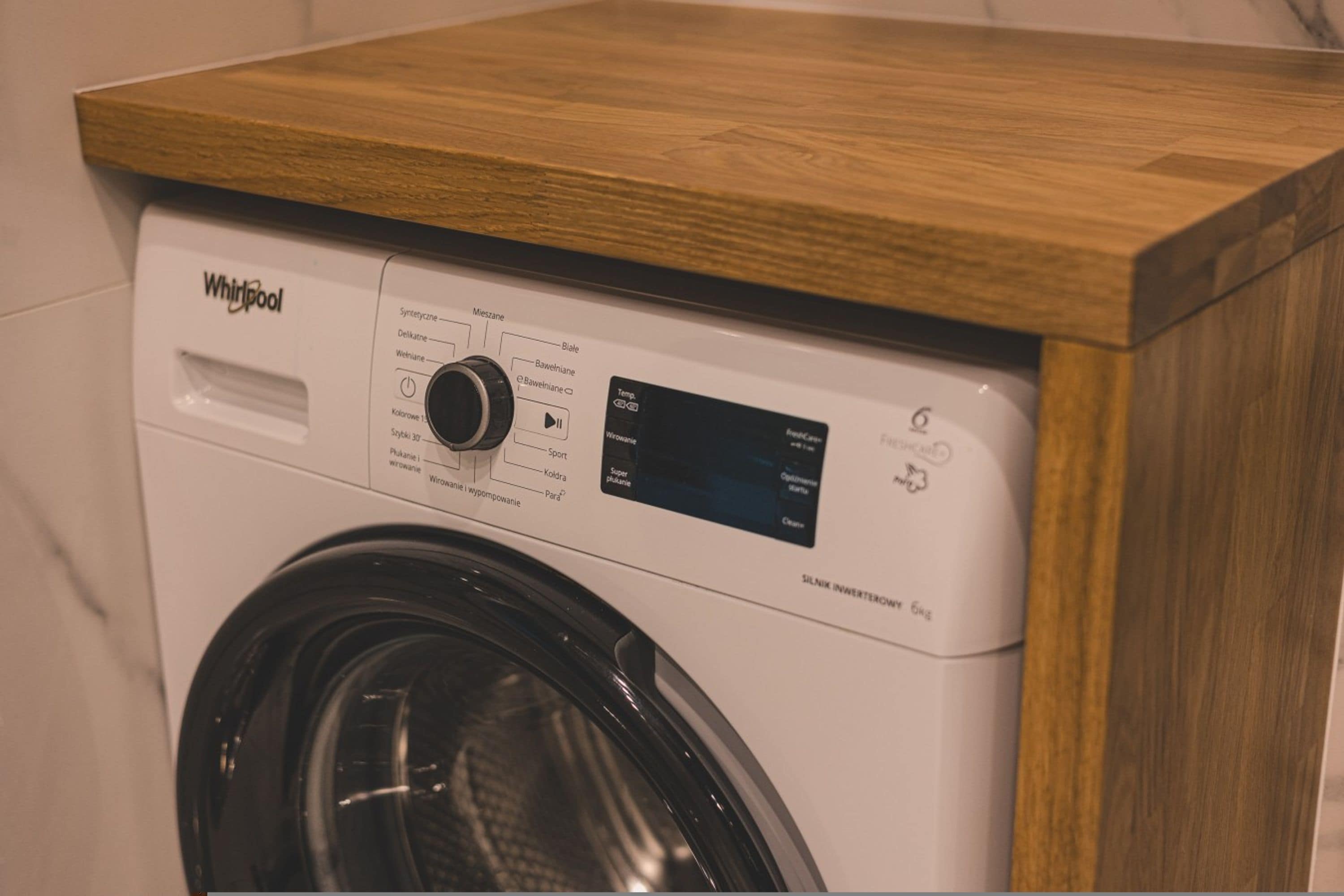 En tvättmaskin från Whirlpool med frontmatning och en bänkskiva i trä.