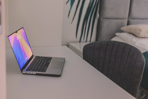 A laptop on a white table with a grey chair beside it.