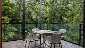 Una terraza exterior con barandilla de vidrio, una mesa y cuatro sillas.