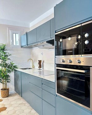 A modern kitchen with grey cabinets, a stainless steel Bosch oven, and a window above the sink. - Family flat for 6 steps from Champs Elysees (Paris)