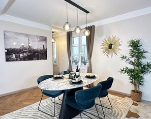 A dining area with a round table, chairs, a cityscape painting, a sunburst mirror, and a potted plant. - Family flat for 6 steps from Champs Elysees (Paris)