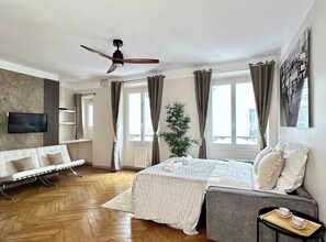 Une chambre moderne avec un lit, un canapé, une télévision, une plante et une fenêtre avec des rideaux.