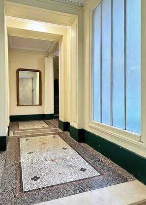 A hallway with a patterned floor, a large mirror, and a window with blinds. - Family flat for 6 steps from Champs Elysees (Paris)