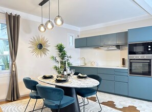 A modern kitchen with a round dining table, blue chairs, a hanging light fixture, and a Bosch oven. - Family flat for 6 steps from Champs Elysees (Paris)