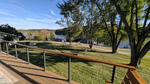 Eine Terrasse mit Geländer, die auf eine Wiese mit Bäumen und ein Gewässer im Hintergrund blickt.