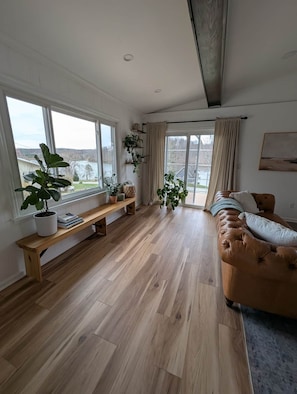 A spacious living room with a wooden floor, a large window, a bench, and a leather sofa. - Lake Haven- a luxurious lakeside retreat on Lake Logan (Falls Township)