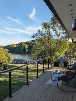 A deck with outdoor furniture overlooking a lake and forested hills. - Lake Haven- a luxurious lakeside retreat on Lake Logan (Falls Township)