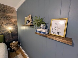 A bedroom with a bed, a nightstand, a wall-mounted shelf with decorative items, and a wall-mounted lamp. - Lake Haven- a luxurious lakeside retreat on Lake Logan (Falls Township)