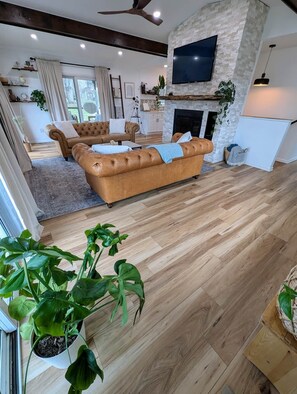 A spacious living room with a large brown leather sofa, a fireplace, and a flat-screen TV mounted on a stone wall. - Lake Haven- a luxurious lakeside retreat on Lake Logan (Falls Township)
