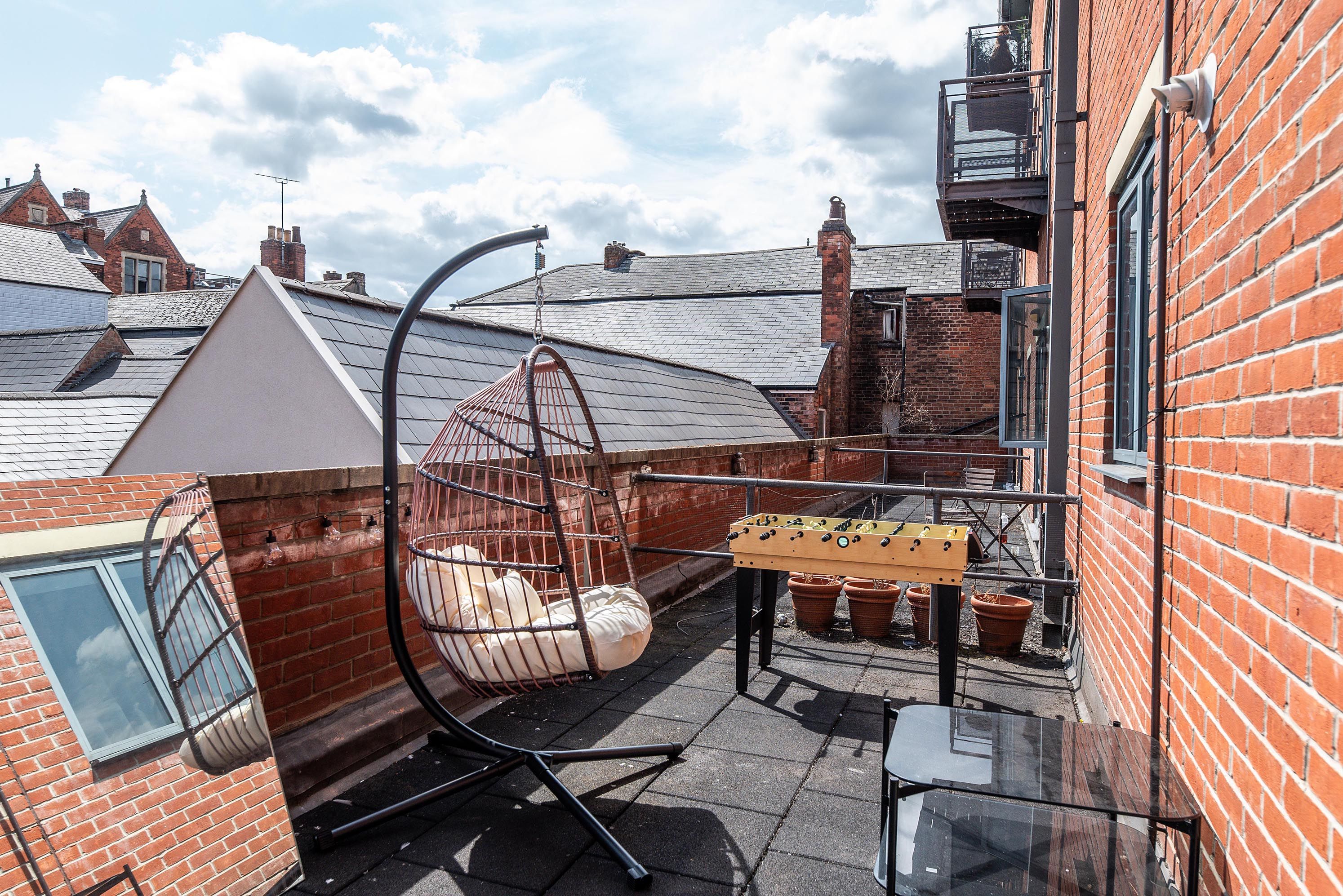 A rooftop terrace with a hanging chair, a foosball table, and a glass table.