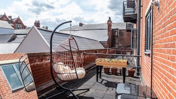 A rooftop terrace with a hanging chair, a foosball table, and a glass table.