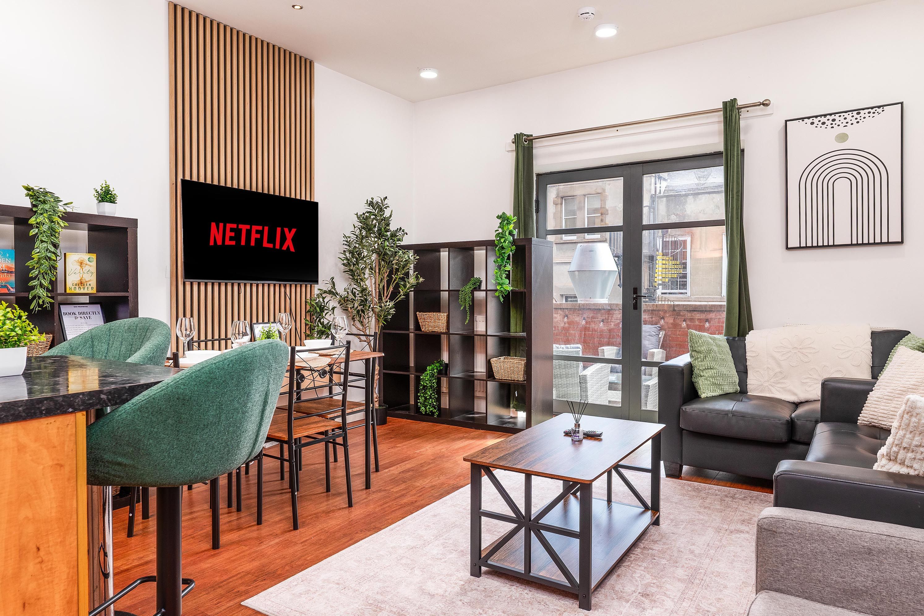 A modern living room with a flat-screen TV, a dining area with chairs, a coffee table, and a sofa.