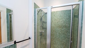 Ein Badezimmer mit Duschkabine aus Glas, grünen Mosaikfliesen und einer weißen Badewanne.