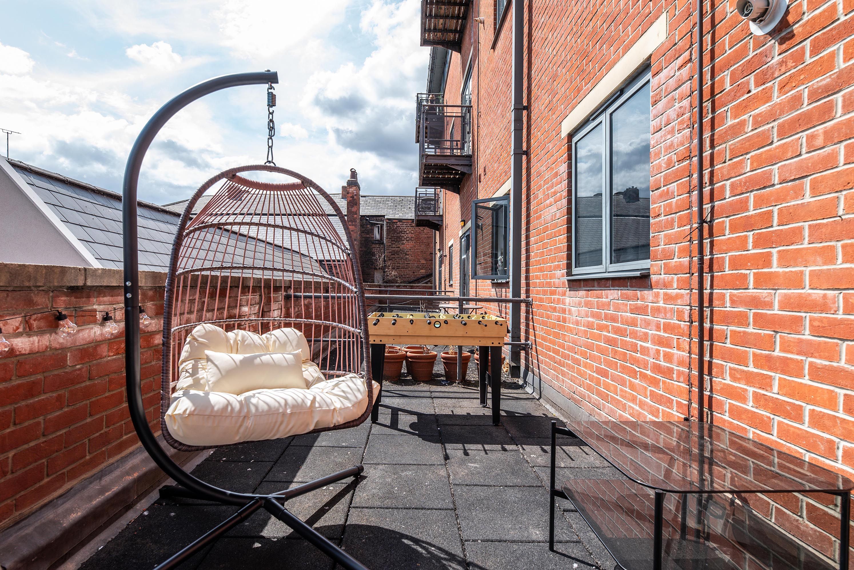 A narrow alleyway with a brick building, a hanging chair, and a foosball table.