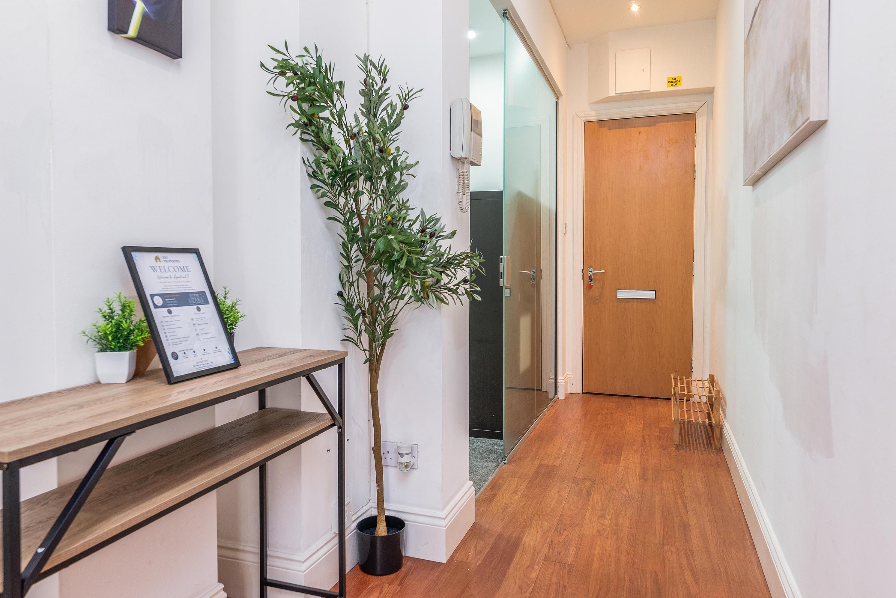 A hallway with a reception desk, a framed welcome sign, a potted plant, and a wooden door.