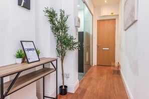 Un pasillo con una recepción, un letrero de bienvenida enmarcado, una planta en maceta y una puerta de madera.