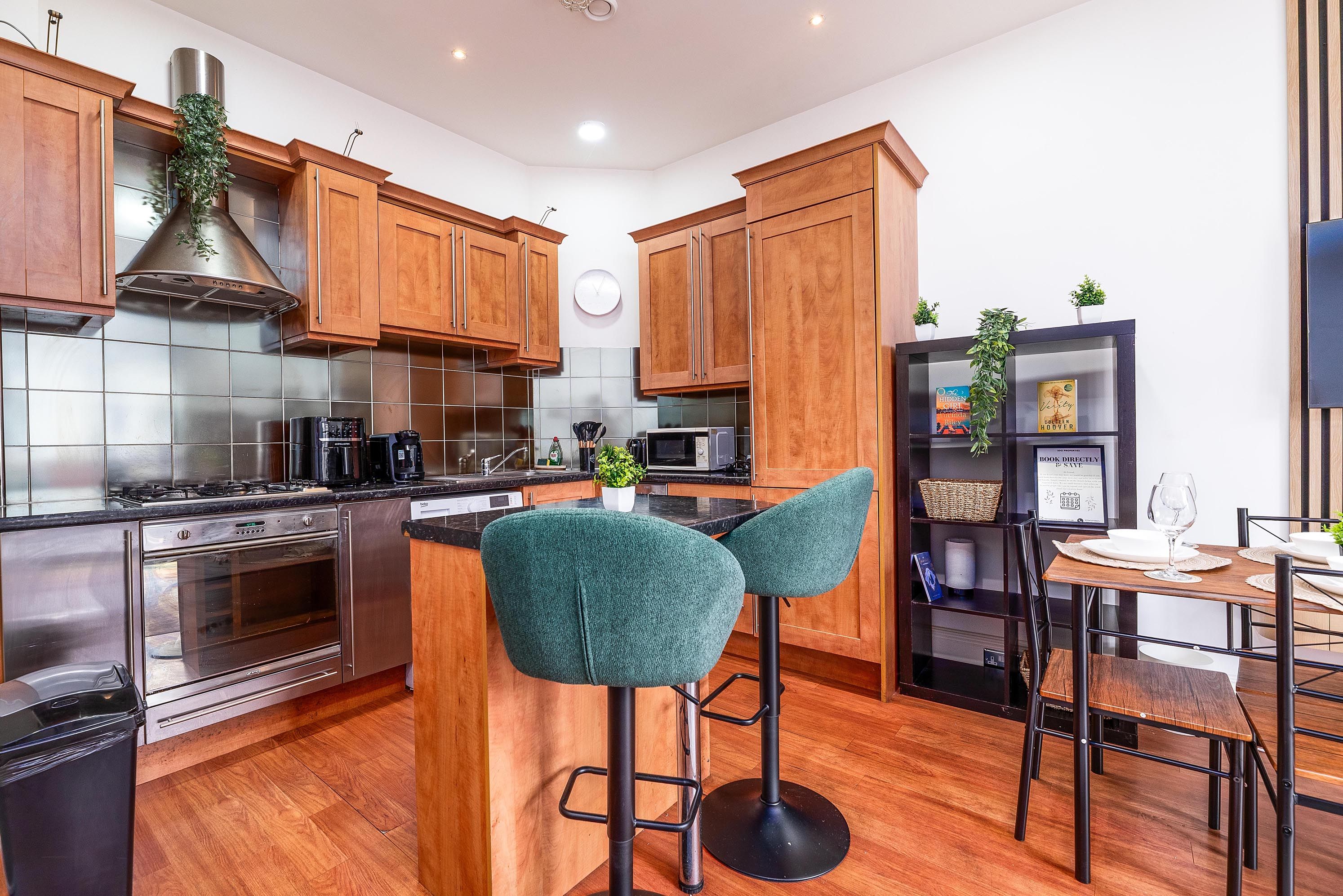 A modern kitchen with wooden cabinets, stainless steel appliances, a central island with bar stools, and a dining area with a table and chairs.