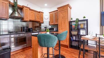 A modern kitchen with wooden cabinets, stainless steel appliances, a central island with bar stools, and a dining area with a table and chairs.