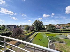 A residential area with a rectangular pond, surrounded by well-maintained hedges and trees, and houses in the background. - Green Lake Retreat with balcony by Interhome (De Haan)