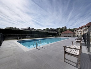 A swimming pool with a tiled deck, metal ladder, and wooden benches. - Green Lake Retreat with balcony by Interhome (De Haan)