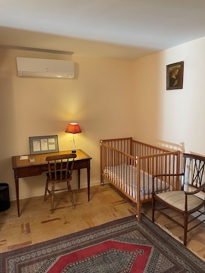 Una habitación con escritorio, silla, cuna y alfombra estampada.