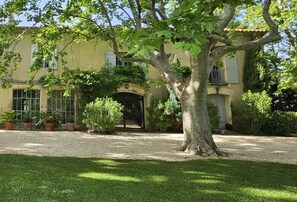 A building with a large tree in the foreground, a gravel driveway, and a well-maintained lawn.