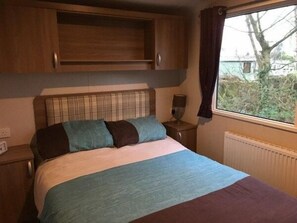Ein Schlafzimmer mit einem Bett, einem Nachttisch, einem Fenster mit Vorhängen und einer Heizung.