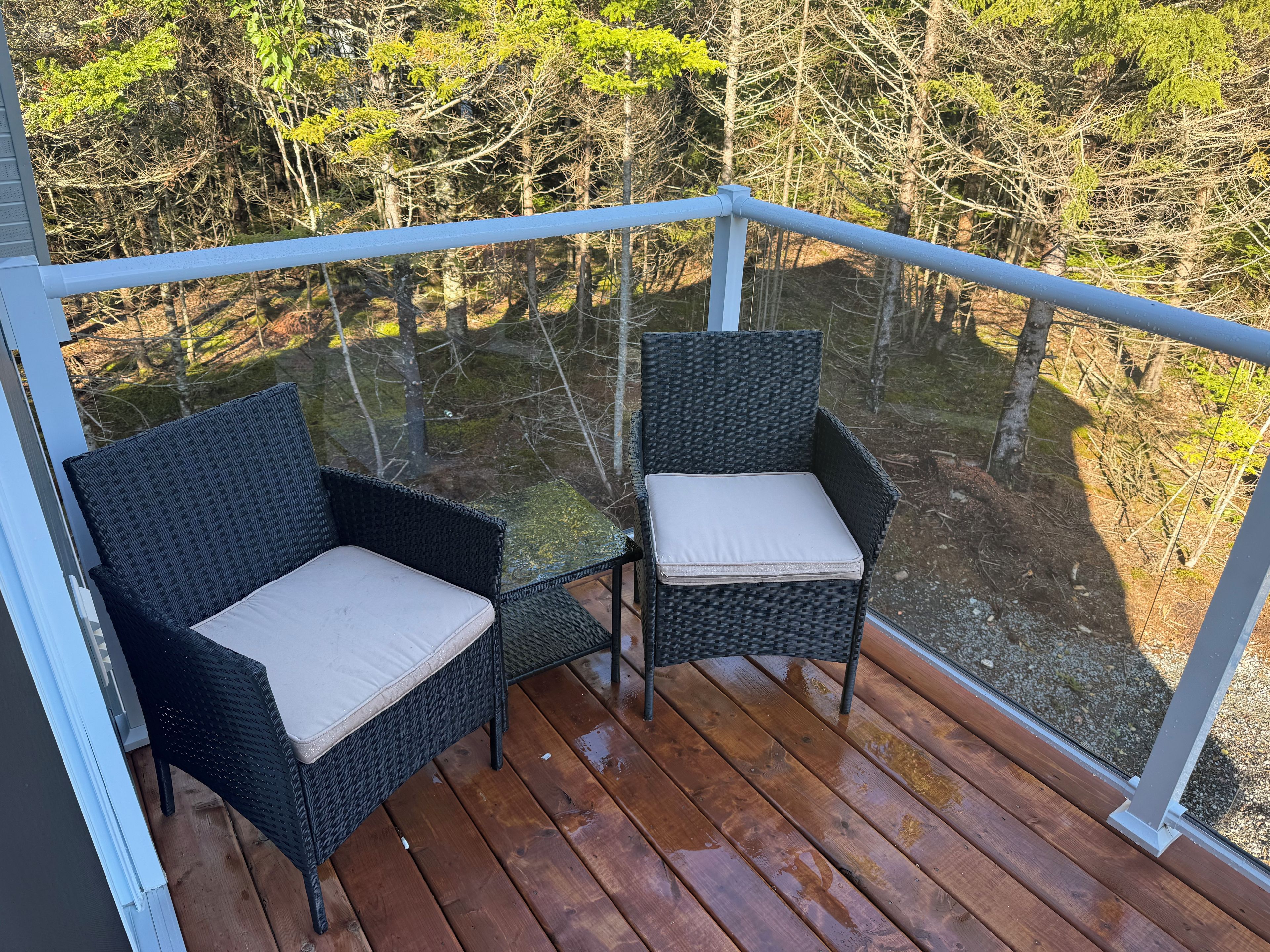 A wooden deck with two wicker chairs and a glass balustrade.