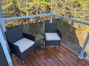 A wooden deck with two wicker chairs and a glass balustrade.