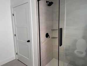 A bathroom with a glass shower enclosure, a white door, and a toilet visible through the glass. - Grandview Haven |3BR Private Retreat (East Uniacke)