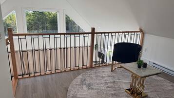 A spacious room with a high ceiling, a wooden railing, a round rug, a table with a gold base, and a black chair.