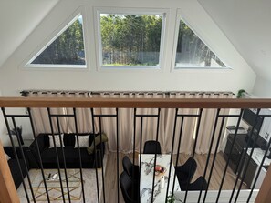 Un espace de vie de style « loft », avec un plafond en pente, un coin repas doté d’une table en marbre et une vue sur une forêt, visible à travers de grandes fenêtres.