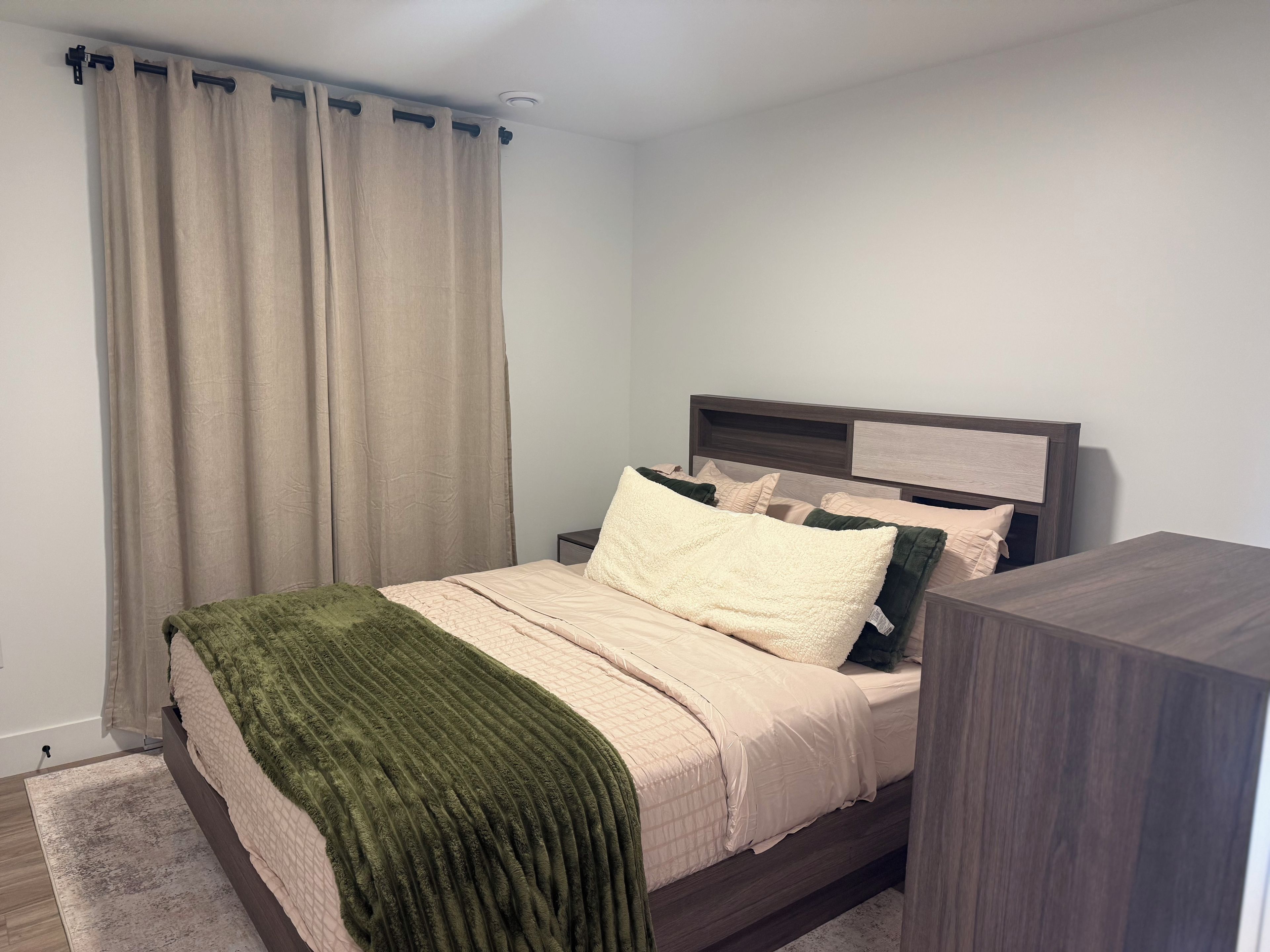 A neatly made bed with a green throw blanket, a wooden headboard, and a bedside table with a lamp.