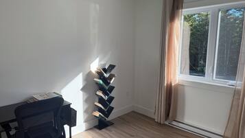 A room with a black office chair, a wall-mounted bookcase, a window with curtains, and a wooden floor.