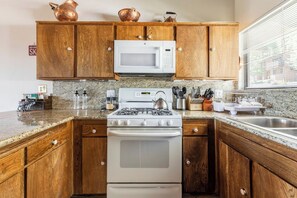 A kitchen with wooden cabinets, a white microwave, a stove, and a granite countertop. - Stunning View Condo: Ski-in, Hot Tub (Mammoth Lakes)