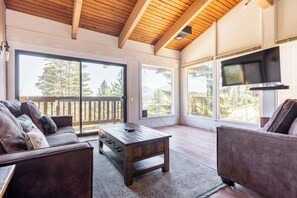 A spacious living area with a wooden ceiling, a large sliding glass door leading to an outdoor deck, and a flat-screen TV mounted on the wall. - Stunning View Condo: Ski-in, Hot Tub (Mammoth Lakes)