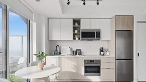 Una cocina moderna con microondas, horno y refrigerador integrados, una mesa de comedor redonda con sillas y vistas a la ciudad a través de amplias ventanas.