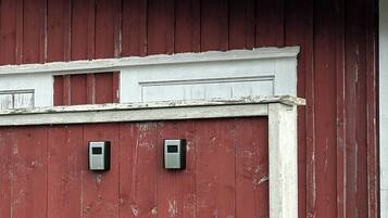 A red barn with a white trim and two small, square, metallic objects mounted on the wall.