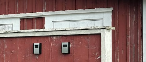A red barn with a white trim and two small, square, metallic objects mounted on the wall.