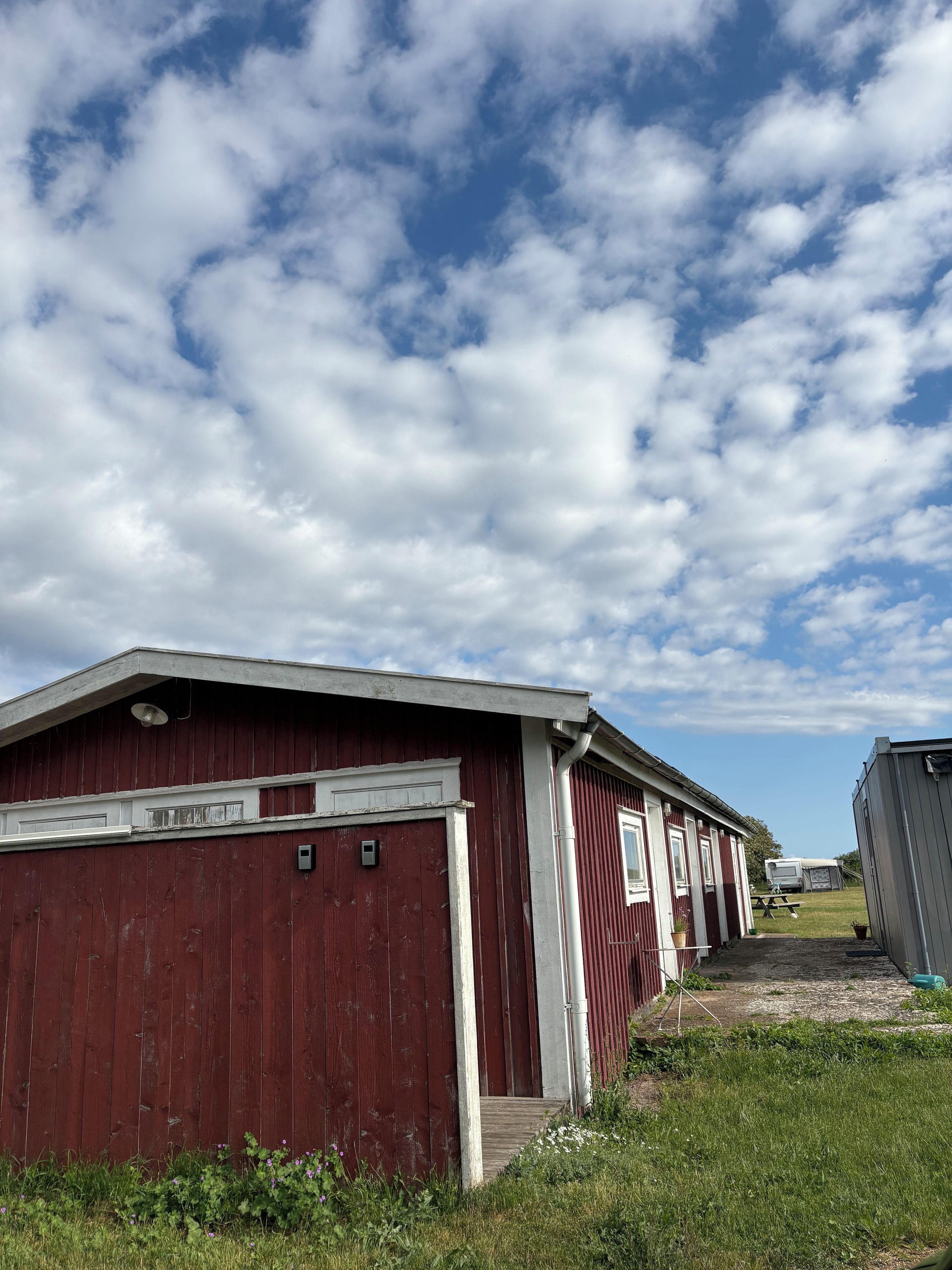 A red barn with a white door and a small porch, surrounded by grass and a clear sky.
