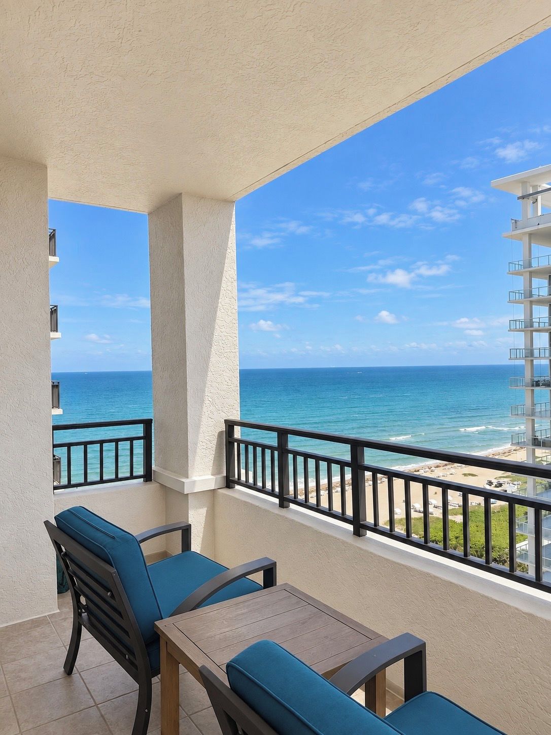 A balcony with a view of the ocean, a table, and two chairs.