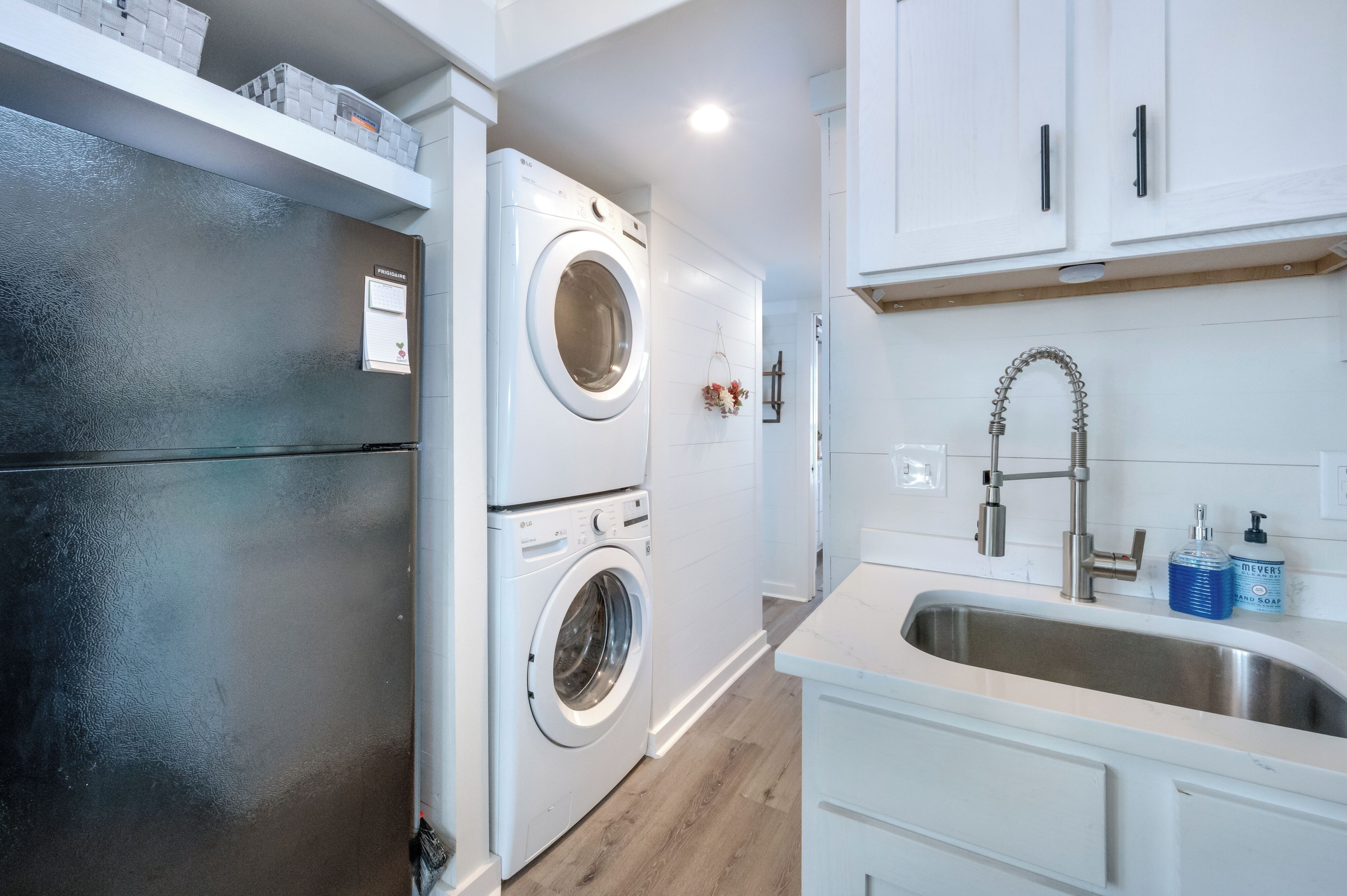 Cocina compacta con lavadora y secadora integradas, pileta de acero inoxidable y muebles de cocina blancos.