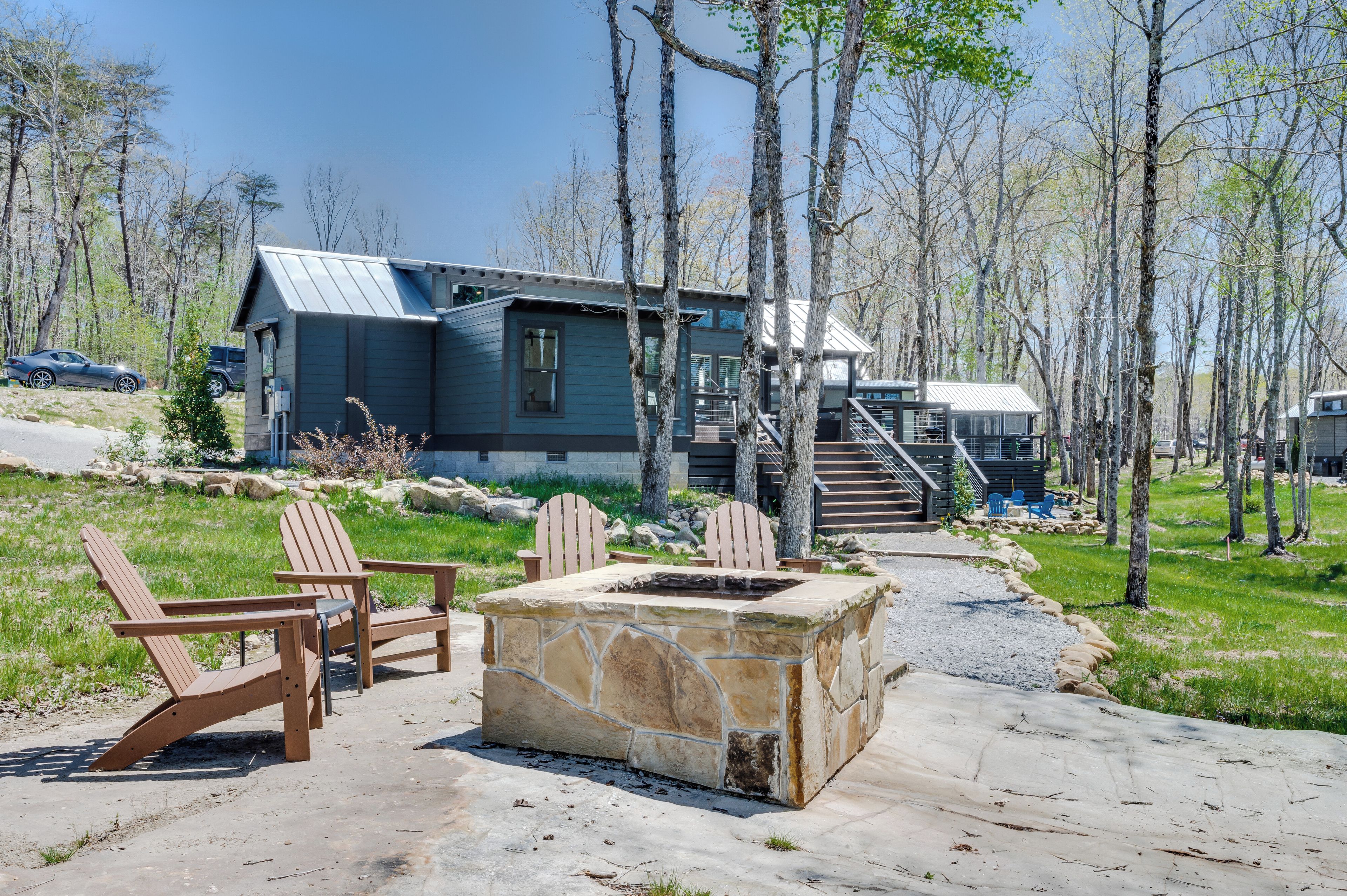 A cabin with a stone fire pit, wooden Adirondack chairs, and a metal staircase leading to a deck.